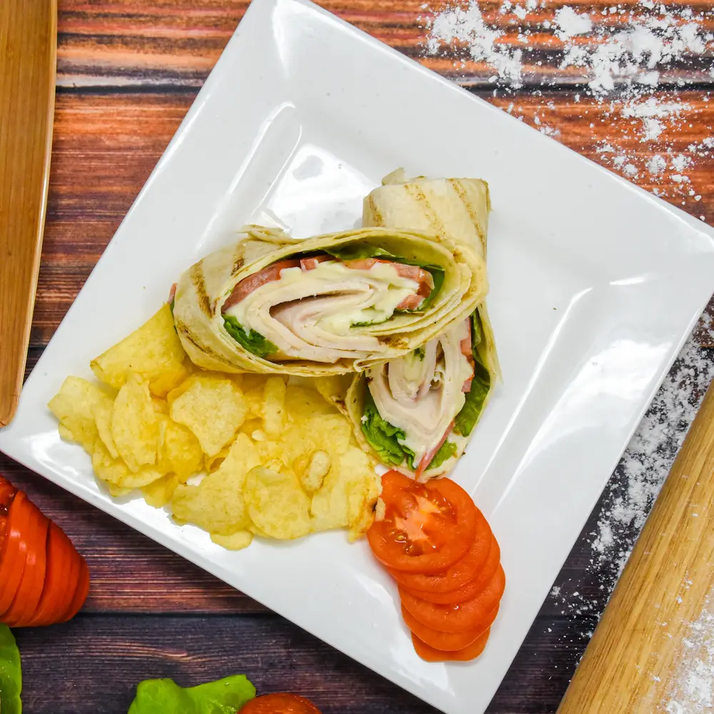 turkey wraps, chips, and tomatoes on a white plate